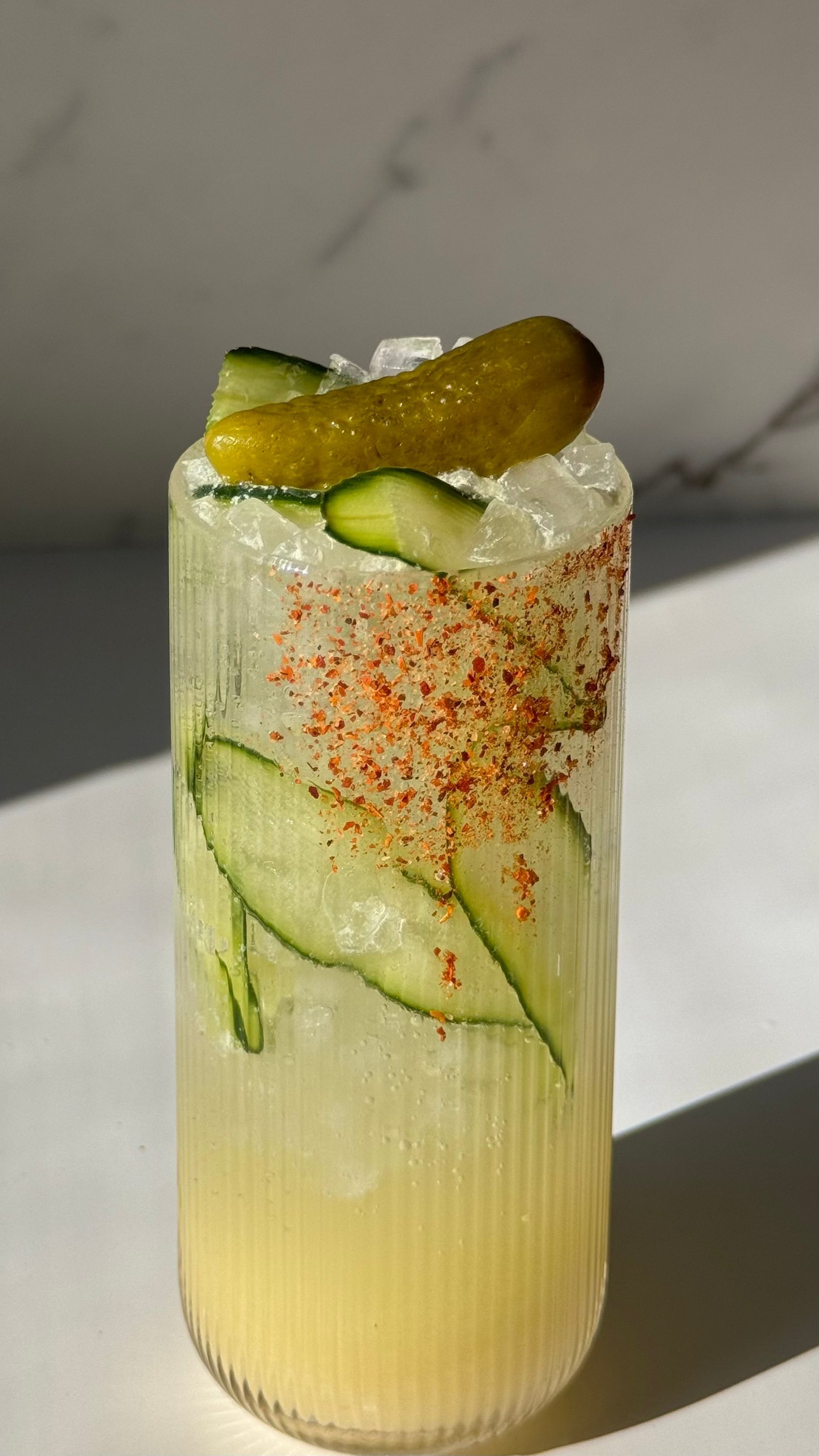 Savory pickle magnesium refresher over ice in a chili-rimmed glass with cucumber slices and a pickle garnish